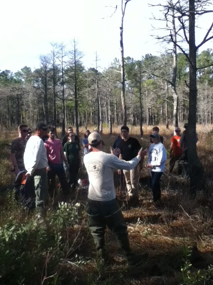 An SCDNR employee standing in front of a group of students outdoors while motioning with his hands mid-explanation.