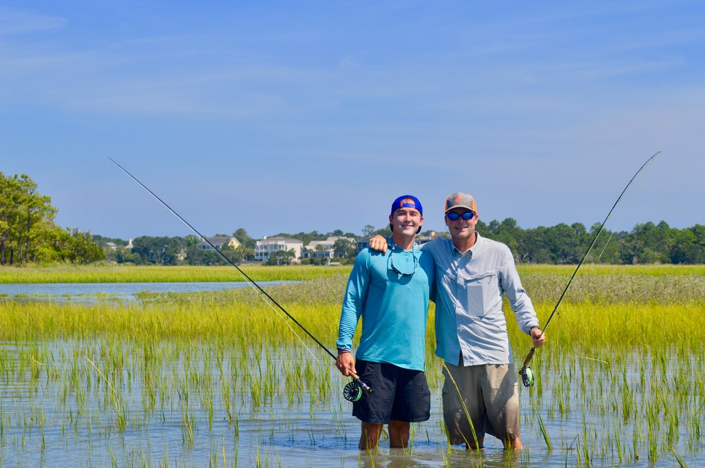 Jackson Bland and his father holding fishing rods standing knee deep in water.